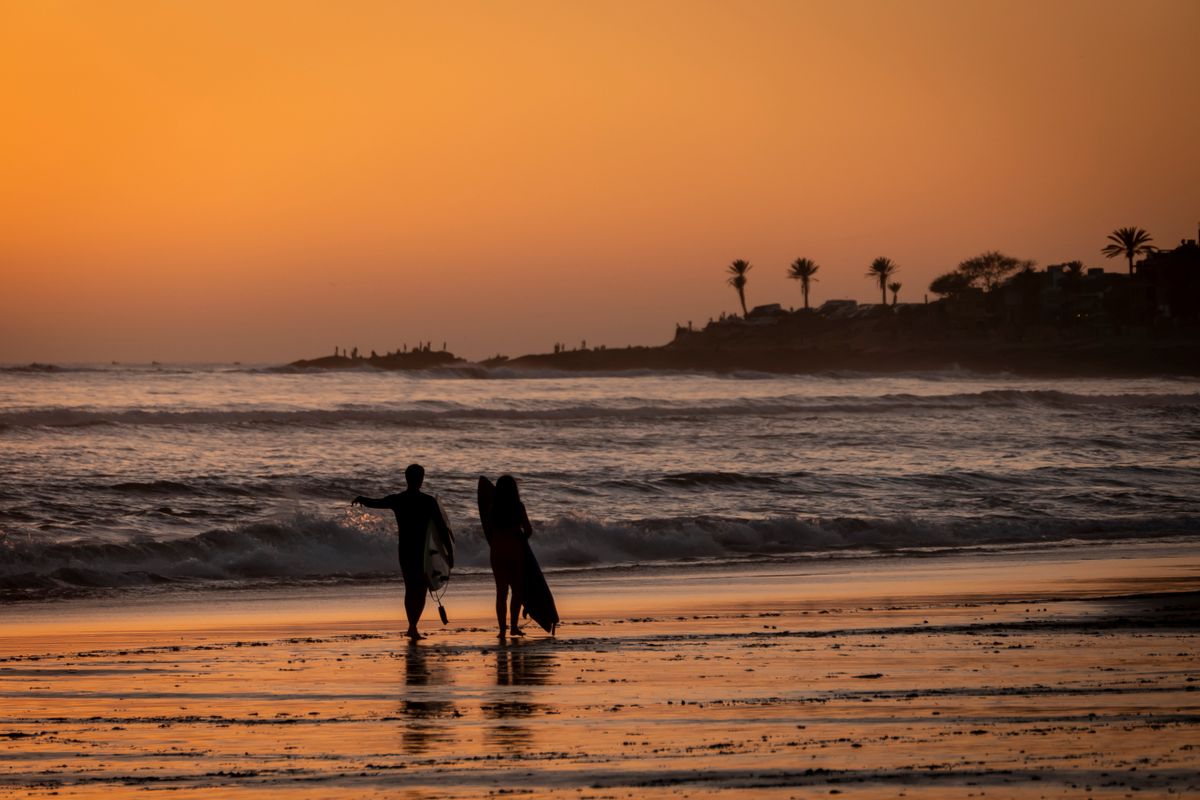 Surfers walking along the Atlantic coast near Taghazout, Morocco at sunset