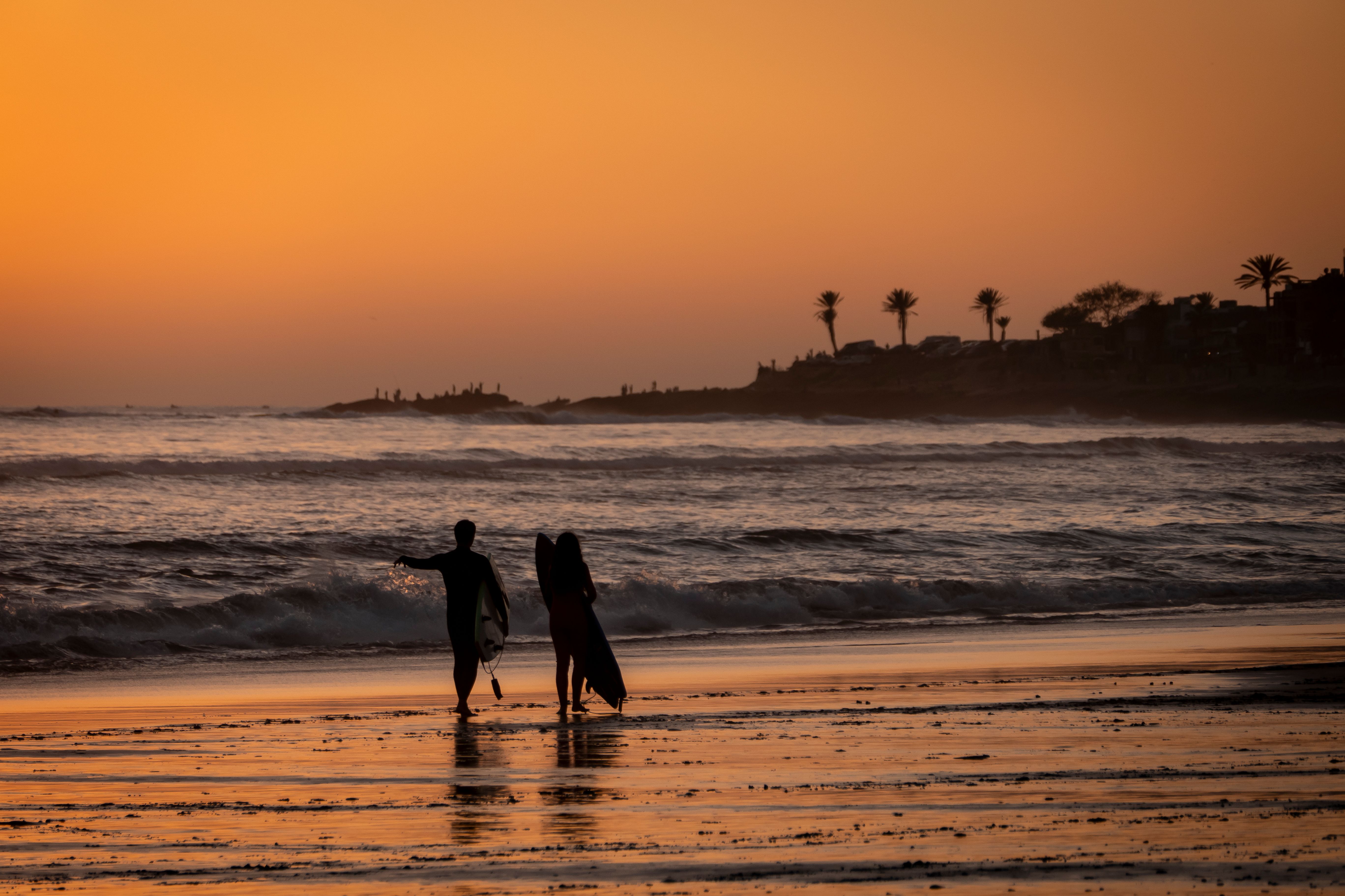 Surfers carrying boards along the Atlantic shoreline in Morocco at sunset