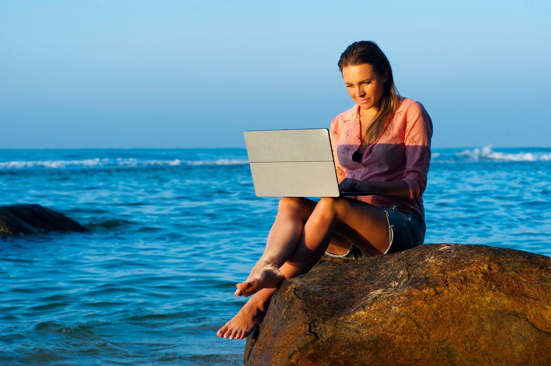 Frau arbeitet mit dem Laptop auf einem Felsen am Meer
