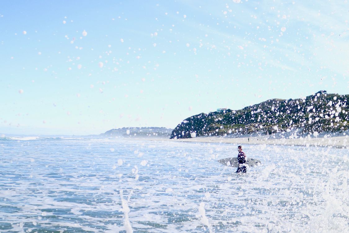 Person traegt ein Surfbrett ins Wasser