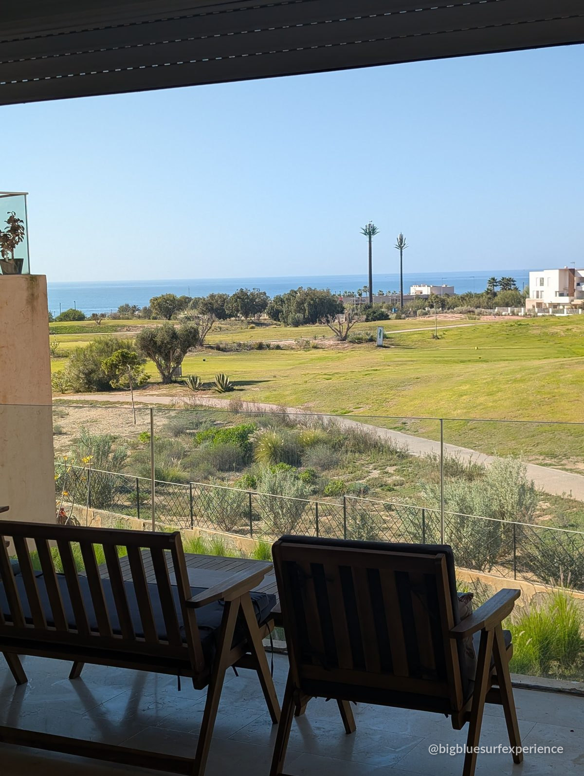 Terrace of the BigBlue Bay Studio with two wooden chairs looking over the golf course to the ocean